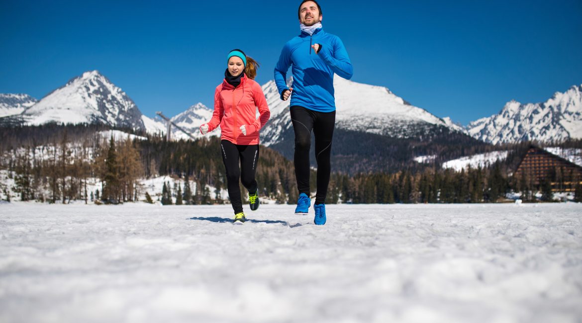 Young couple jogging outside in sunny winter mountains.