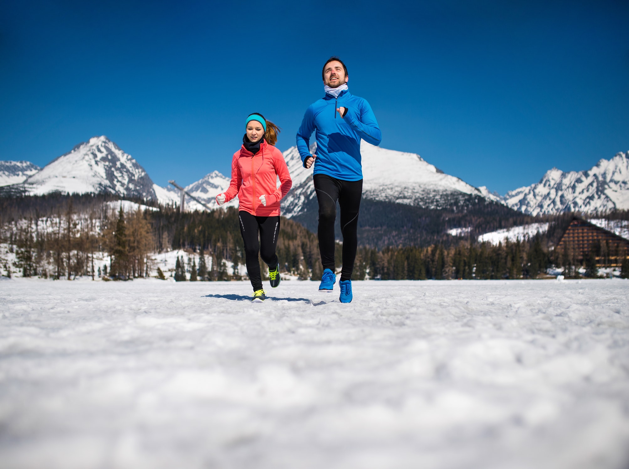 Young couple jogging outside in sunny winter mountains.
