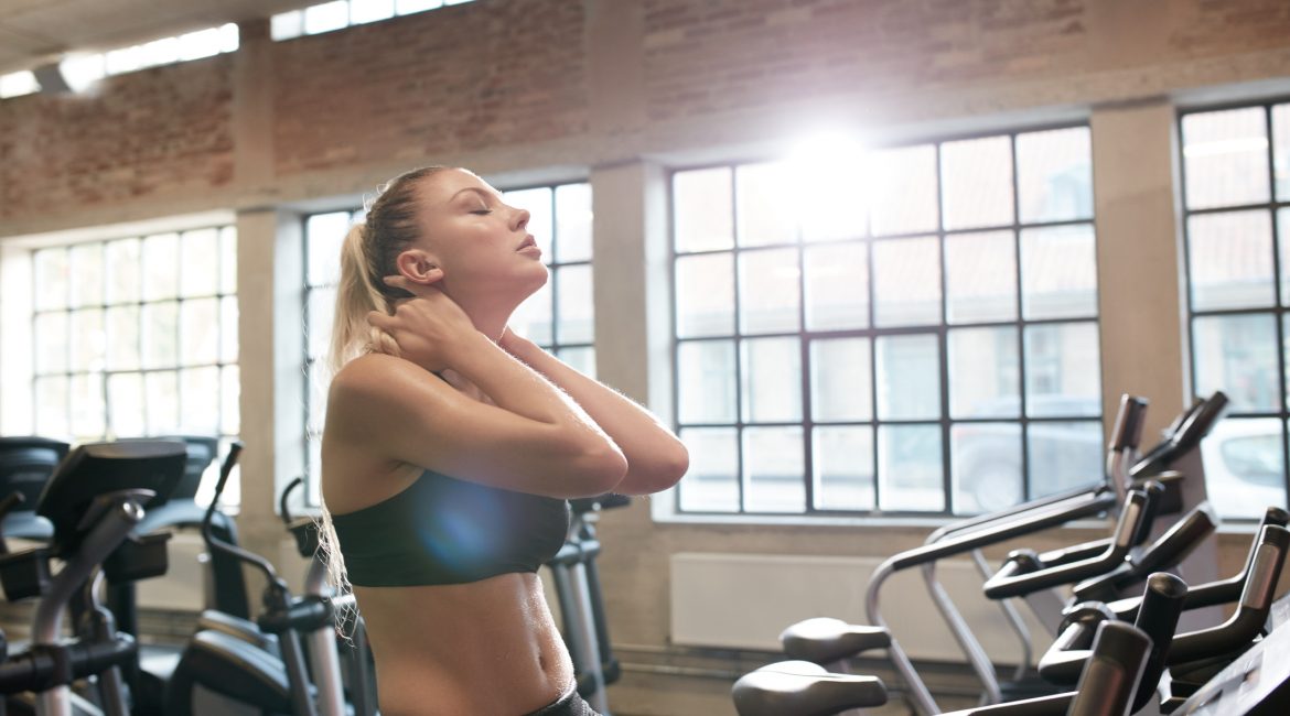 Young woman tired after intense workout on gym bike. Relaxing her neck muscles after workout in fitness club.
