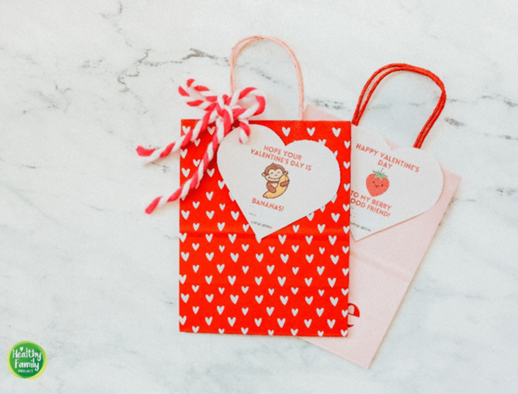 One festive red Valentine's Day bag with Crispy Green imagery attached to it on top of a festive pink Valentine's Day bag with Crispy Green imagery attached to it.