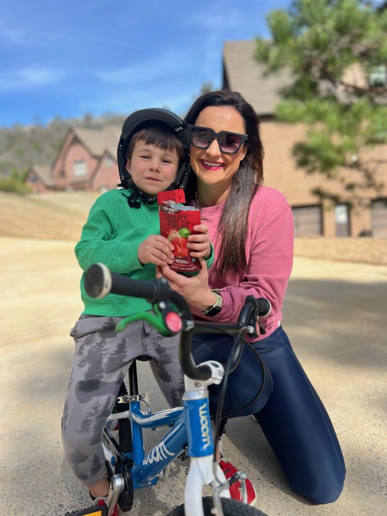 Mother and kid posing outside with Crispy Fruit apple. The kid is on a bike.